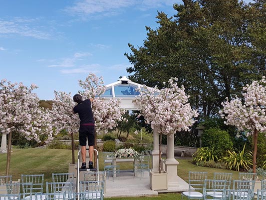 Ornatmental handmade blossom trees being assembled outside for a garden wedding ceremony