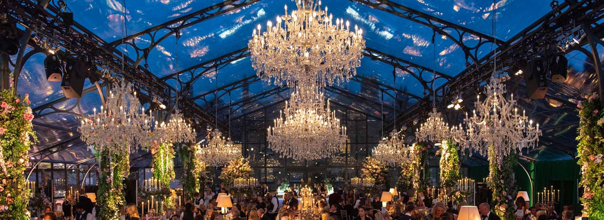 Marie Therese chandeliers adorn the glass ceiling of a marquee for a charity fundraising event